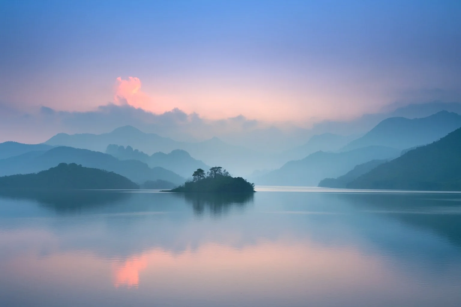 Serene mountain lake at dawn with misty peaks and a small island